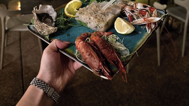 A plat de marisc amb llagosta, ostres i peix, sostingut per una persona que porta un rellotge.