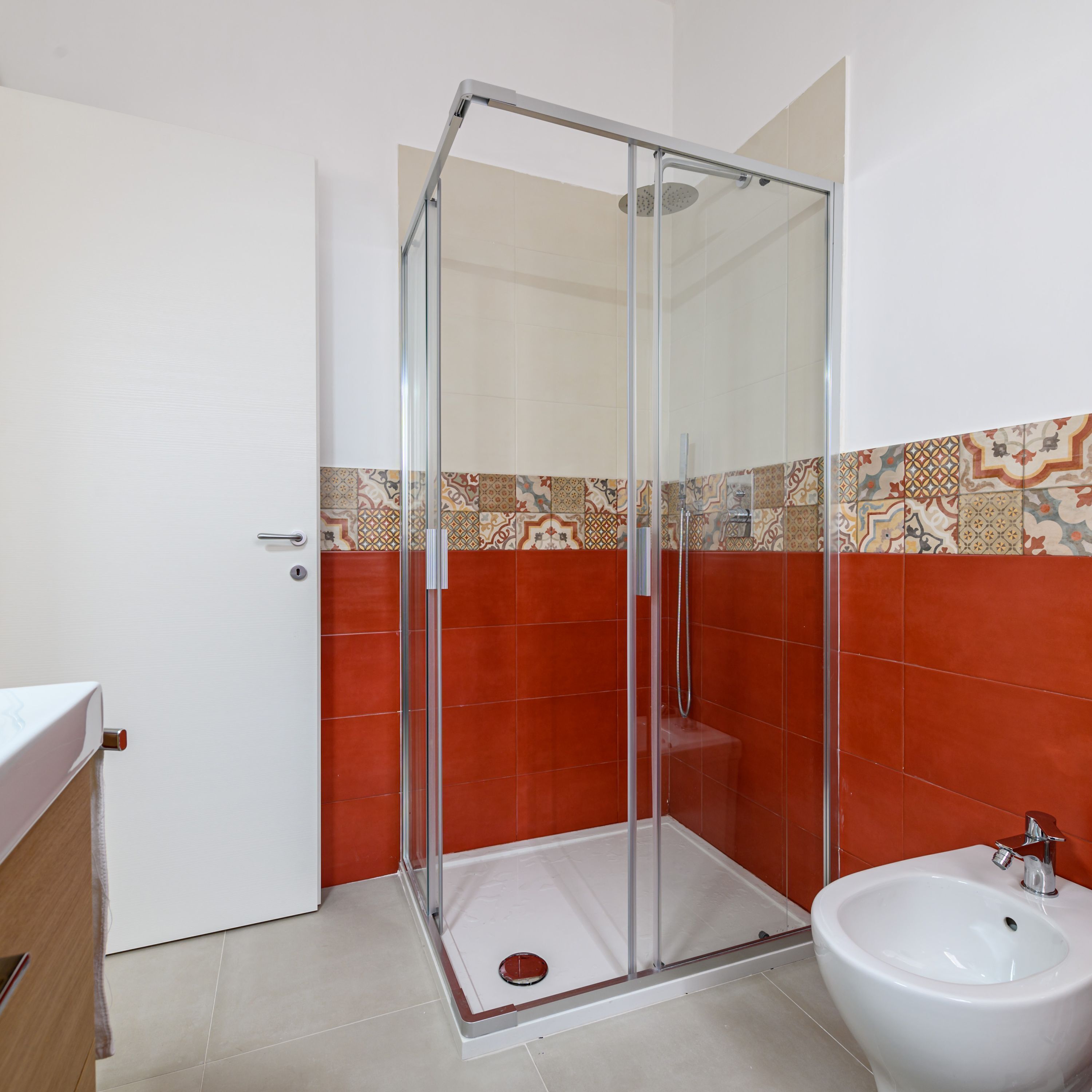 Une salle de bain avec une douche à parois de verre, un lavabo blanc et une zone de douche carrelée.
