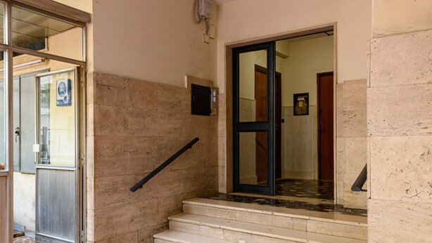 A staircase with a handrail, a door with a glass panel, and a tiled floor. - Via Coriolano 8 in Naples (Naples)
