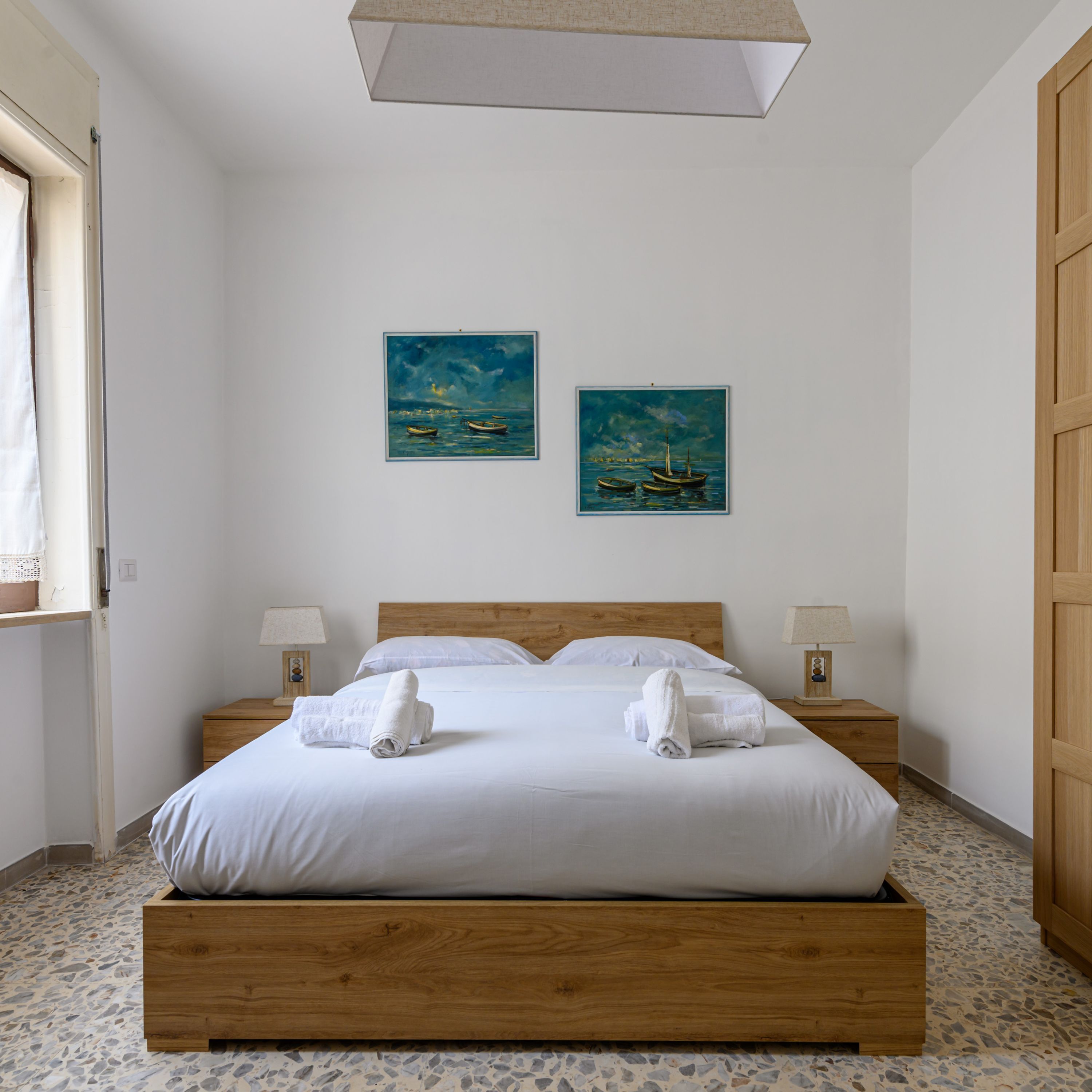A bedroom with a wooden bed, two paintings on the wall, and a window with curtains.