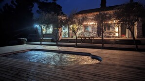 Une terrasse en bois avec un jacuzzi, un mur en pierre et un bâtiment doté d’un espace extérieur aménagé avec des sièges et des éclairages.