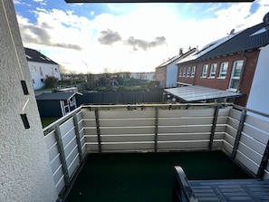 Blick von einem Balkon mit Metallgeländer auf ein Wohngebiet mit Häusern und einem eingezäunten Garten.