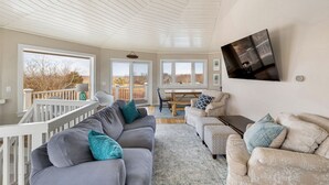 A spacious living room with a high ceiling, large windows, and a comfortable seating area. - Block Island - 4 Bedroom Home on West Beach Road w/ Panoramic Ocean Views + AC! (New Shoreham)
