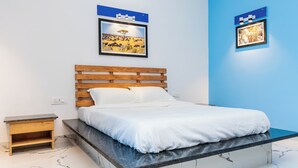 A bedroom with a wooden bed, a nightstand, a marble floor, and two framed pictures on the wall. - Panism Lifestyle (Vanur)