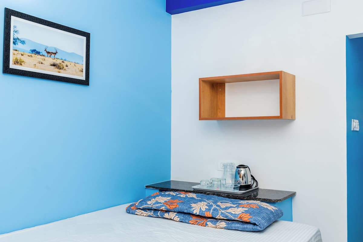 Une pièce comprenant un lit, une armoire en bois, une étagère avec une bouilloire et un tableau encadré accroché au mur.