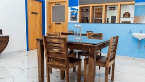A dining area with a wooden table and chairs, a blue accent wall, and a white sink. - Panism Lifestyle (Vanur)