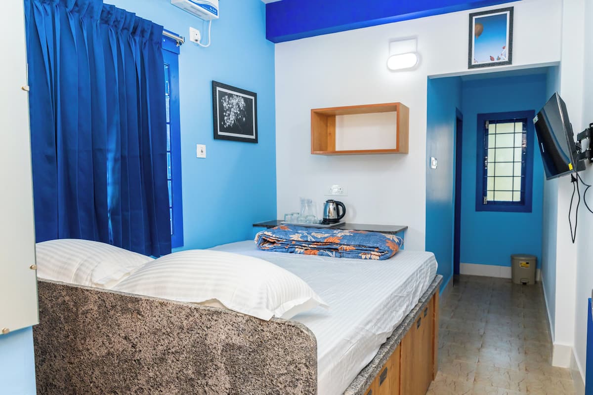 Une chambre avec un lit, une petite table sur laquelle se trouve une bouilloire, un tableau accroché au mur et un téléviseur fixé au mur.
