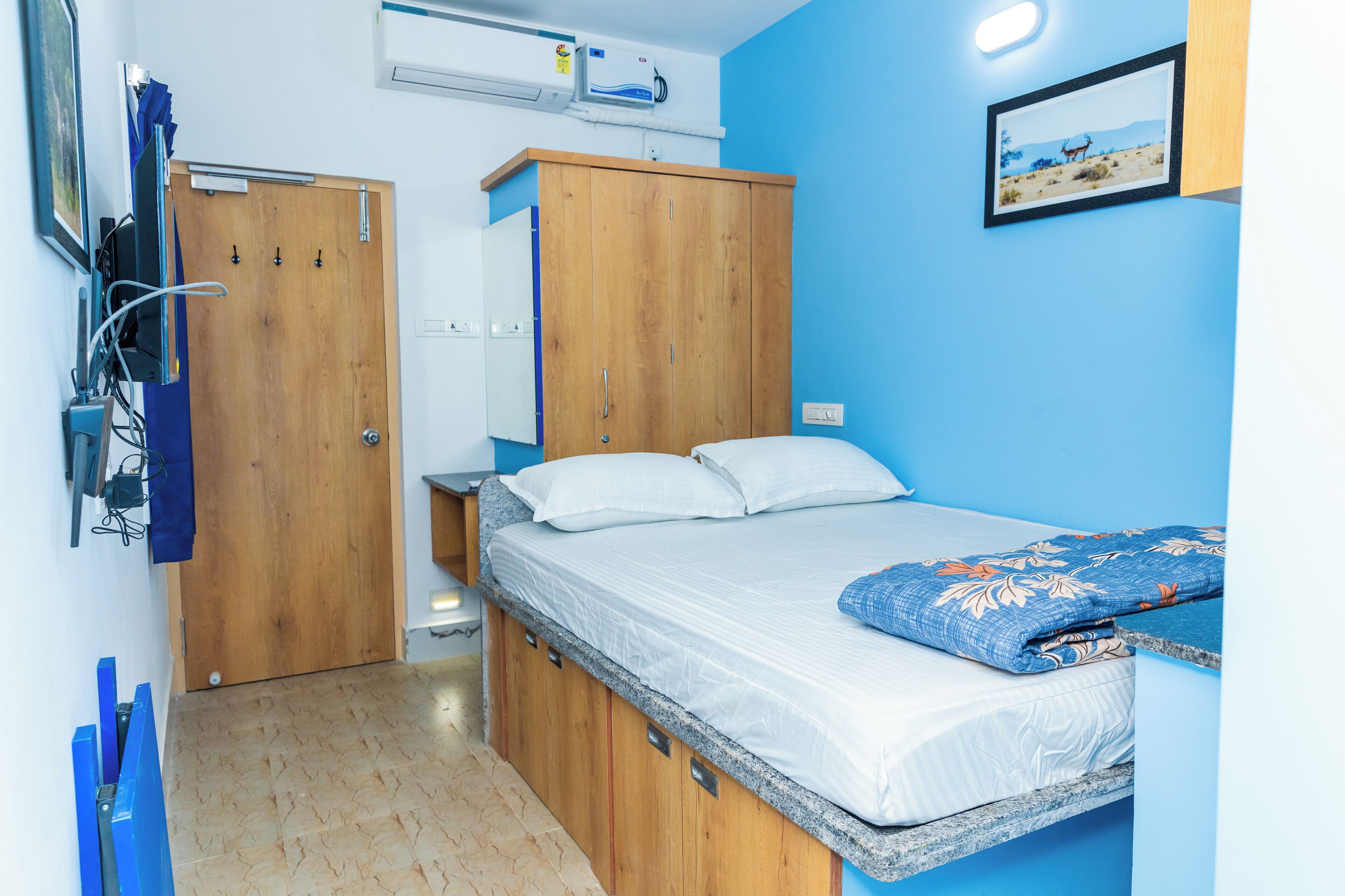A bedroom with a bed, wooden wardrobe, and a wall-mounted air conditioner.