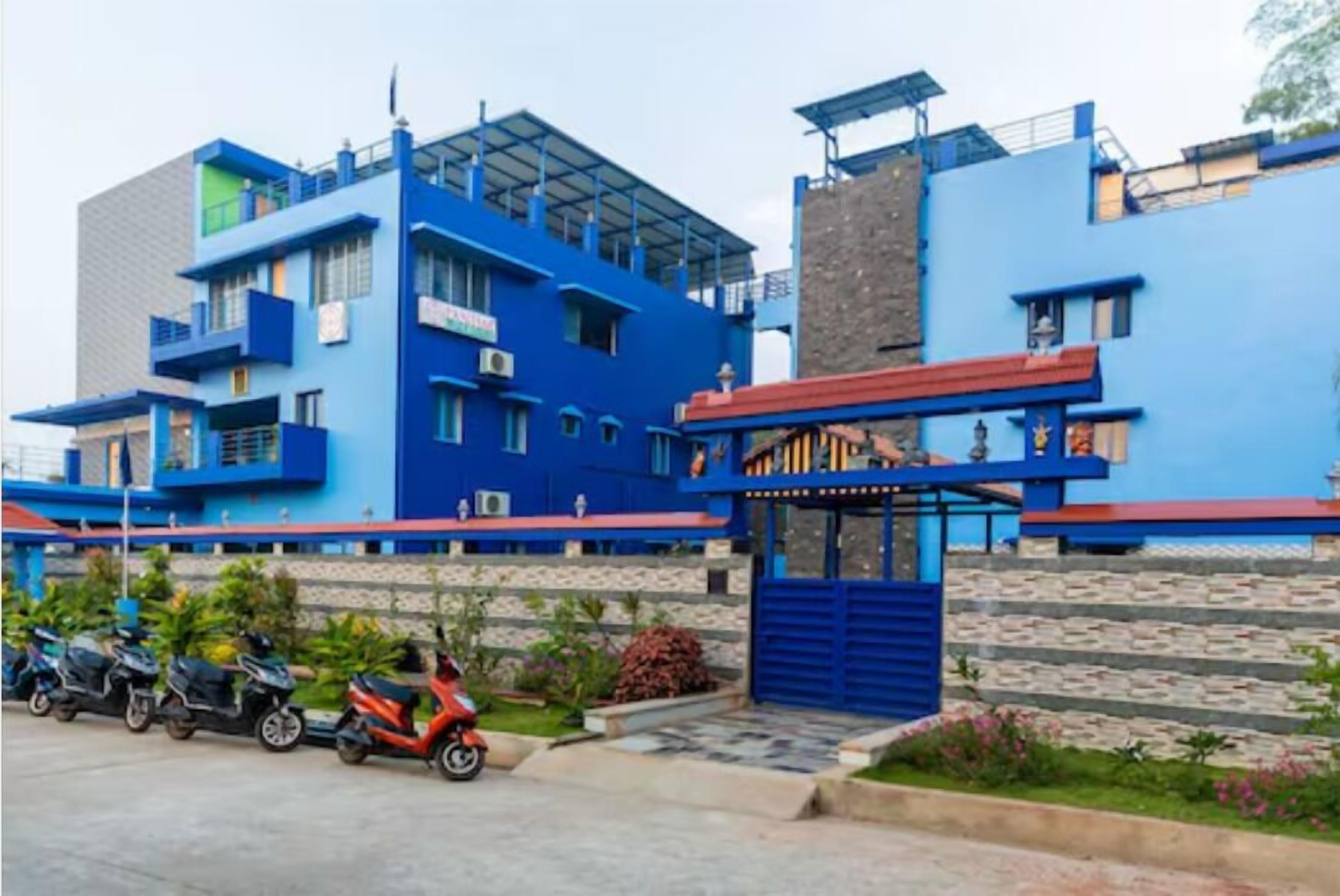 A multi-story building with a blue facade, a gated entrance, and a parking area with scooters.