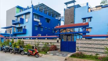 A multi-story building with a blue facade, a gated entrance, and a parking area with scooters.