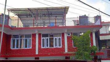 A two-story building with a red and white facade, a balcony on the upper floor, and a blue sign indicating a guest house.