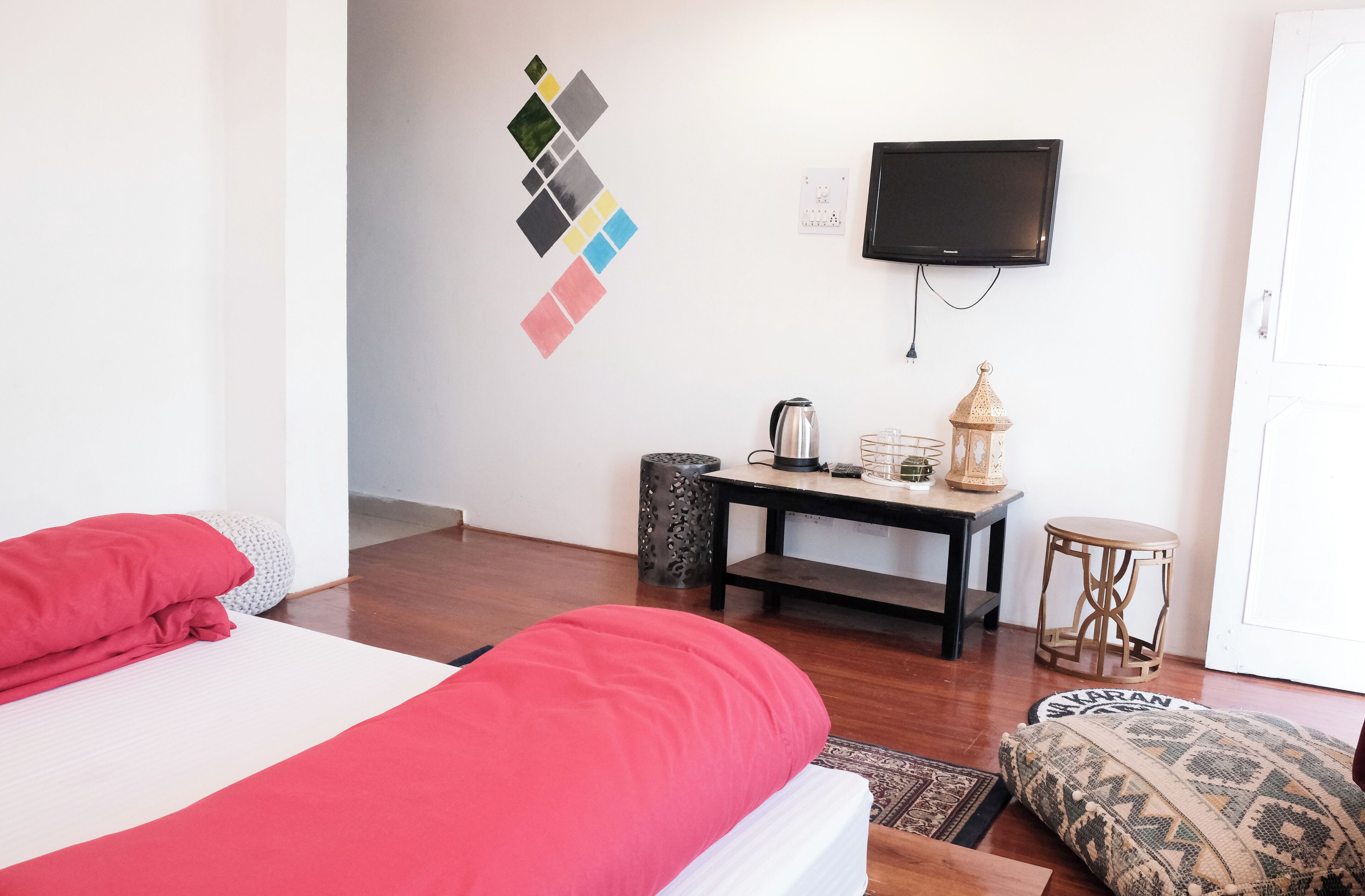 A hotel room with a bed, a TV, a small table with a lamp, and a decorative wall piece.