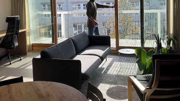 A modern living room with a sofa, a dining table, and a balcony with a view of buildings. - Seaside paradise (Palanga)