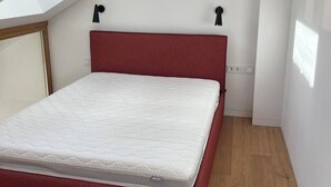 A small, single-bed room with a sloped ceiling and skylight, wooden flooring, and a red bed frame. - Seaside paradise (Palanga)