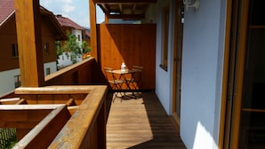 Un balcón de madera con una mesa y sillas, baranda de madera, y vista a edificios vecinos.