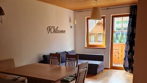 Un cuarto acogedor con techo de madera, una mesa de comedor con sillas, un sofá y una ventana con vistas a edificios.