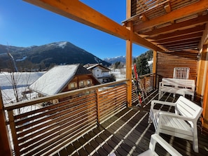 A wooden deck with a view of snow-covered mountains and houses.