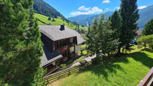 Una casa con techo inclinado, rodeada de exuberantes campos verdes y montañas.