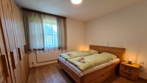 Un dormitorio con una cama de madera, una mesita de noche con lámpara y una ventana con cortinas.