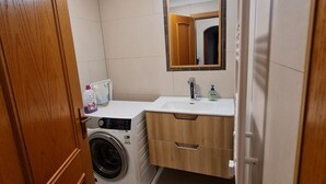 Un baño pequeño con lavadora, lavamanos y espejo.
