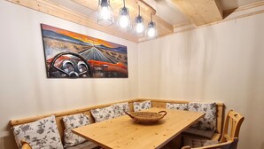 A corner dining area with a wooden table and bench seating, a woven basket on the table, and a painting of a car on the wall. - Die Alte Scheune by Globalimmoservice (Bad Kleinkirchheim)
