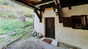Una struttura in legno rustica con una porta e un piccolo oblò, immersa in un vialetto di ghiaia e verde circostante.