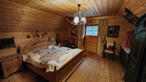 Camera da letto in una baita di legno, con un letto, pareti in legno, un lampadario, una finestra e uno specchio.