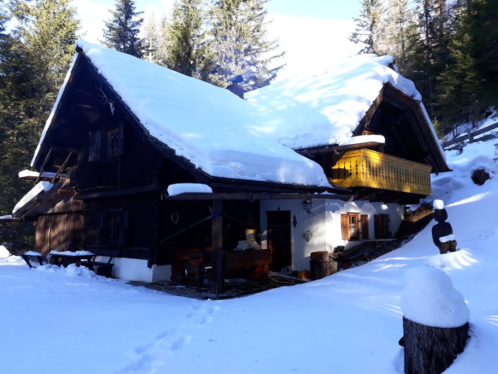 Une cabane en bois, dont le toit est recouvert de neige, entourée d’arbres.