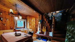 Interno accogliente di una baita rustica con un tavolo da pranzo in legno, sedie, un lampadario e una chitarra appesa al muro.