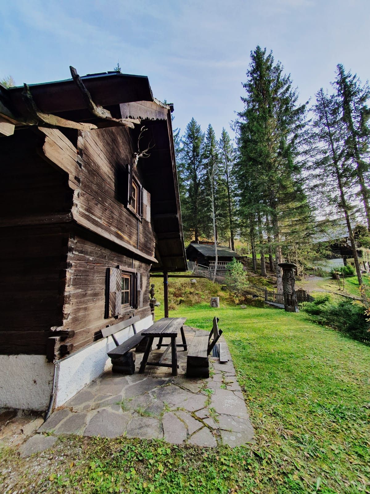 Une cabane rustique en bois, dotée d’un patio pavé de pierres et d’un banc en bois.
