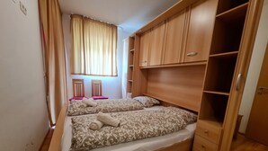 Ein Schlafzimmer mit einem Bett, zwei Stühlen, einem Kleiderschrank und einem Fenster mit Vorhängen.