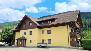 Ein zweistöckiges Gebäude mit gelbem Mauerwerk und braunem Dach, ausgestattet mit zahlreichen Fenstern und einer kleinen angebauten Garage.