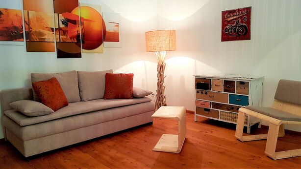 Ein Wohnzimmer mit einer Couch, einem kleinen Tisch, einer Lampe und einer Kommode mit Schubladen.