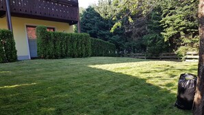 Ein gepflegter Rasen mit Holzzaun, ein Gebäude mit gelber Fassade und ein schwarzer Müllsack in der Nähe eines Baumes.