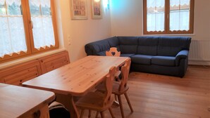 A cozy room with a wooden table and chairs, a dark blue sofa, and a window with curtains.