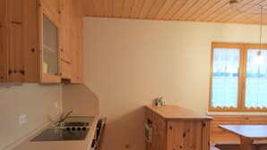 A compact kitchen with wooden cabinets, a built-in stove, and a window with curtains.
