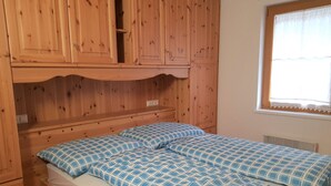 A wooden cabin-style bedroom with a bed, a window with lace curtains, and built-in wooden cabinets.