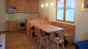 A wooden kitchen with a dining table and chairs, a window with curtains, and hanging light bulbs.
