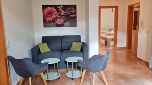 Een woonkamer met een donkerblauwe bank, twee grijze stoelen en een kleine ronde tafel. Een schilderij van roze bloemen hangt aan de muur.