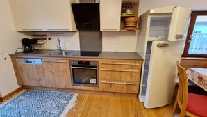 Eine kompakte Küche mit Geschirrspüler, Backofen und integriertem Kochfeld. Auf einem Regal befinden sich ein kleines Spülbecken und ein Wasserkocher.