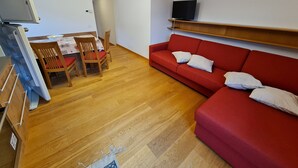 Ein kompakter Wohnraum mit Essbereich, einem roten Sofa und einem an der Wand befestigten Fernseher.