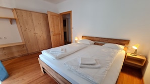 A wooden bed with white linens and two bedside lamps, a wooden wardrobe, and a wooden floor.