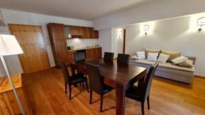 A dining area with a wooden table and chairs, a sofa, and a kitchen in the background.