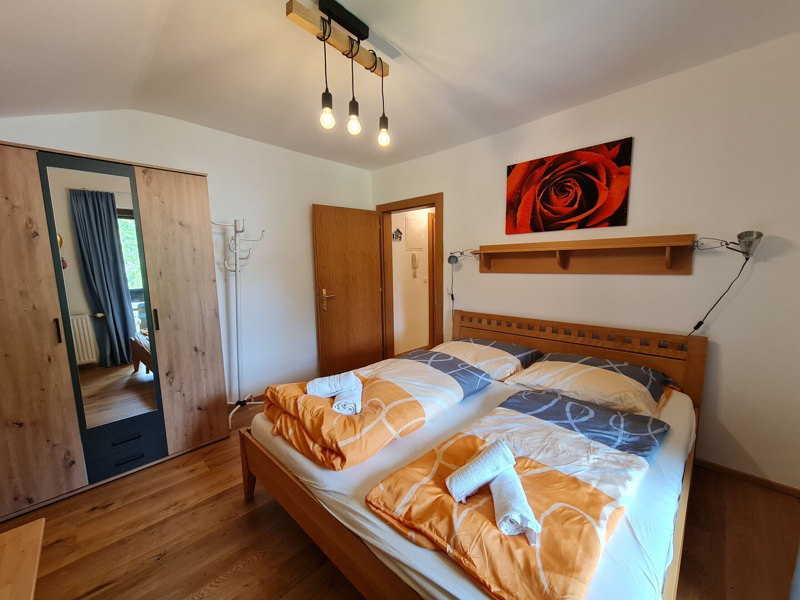 Une chambre à coucher avec un lit en bois, un miroir, une porte et un tableau représentant une rose.