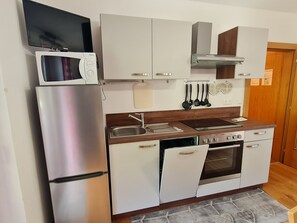 A compact kitchen with a refrigerator, microwave, stove, oven, and a sink.