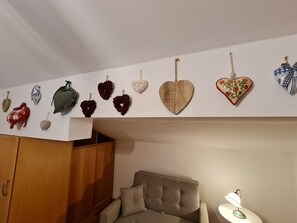 A room with a wooden wardrobe, a grey sofa, and a table with a lamp.