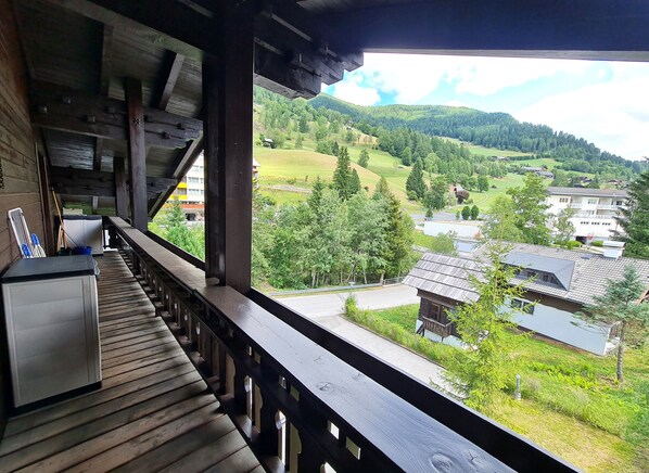 A wooden balcony with a view of a green valley and buildings.