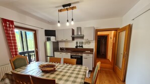 Una cucina compatta con mobili bianchi, un forno a microonde, un frigorifero e un lavello. C'è un tavolo da pranzo con tovaglia a quadri e sedie di legno.