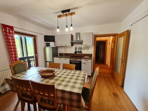 A compact kitchen with white cabinets, a microwave, a refrigerator, and a sink. There is a dining table with a checkered tablecloth and wooden chairs.