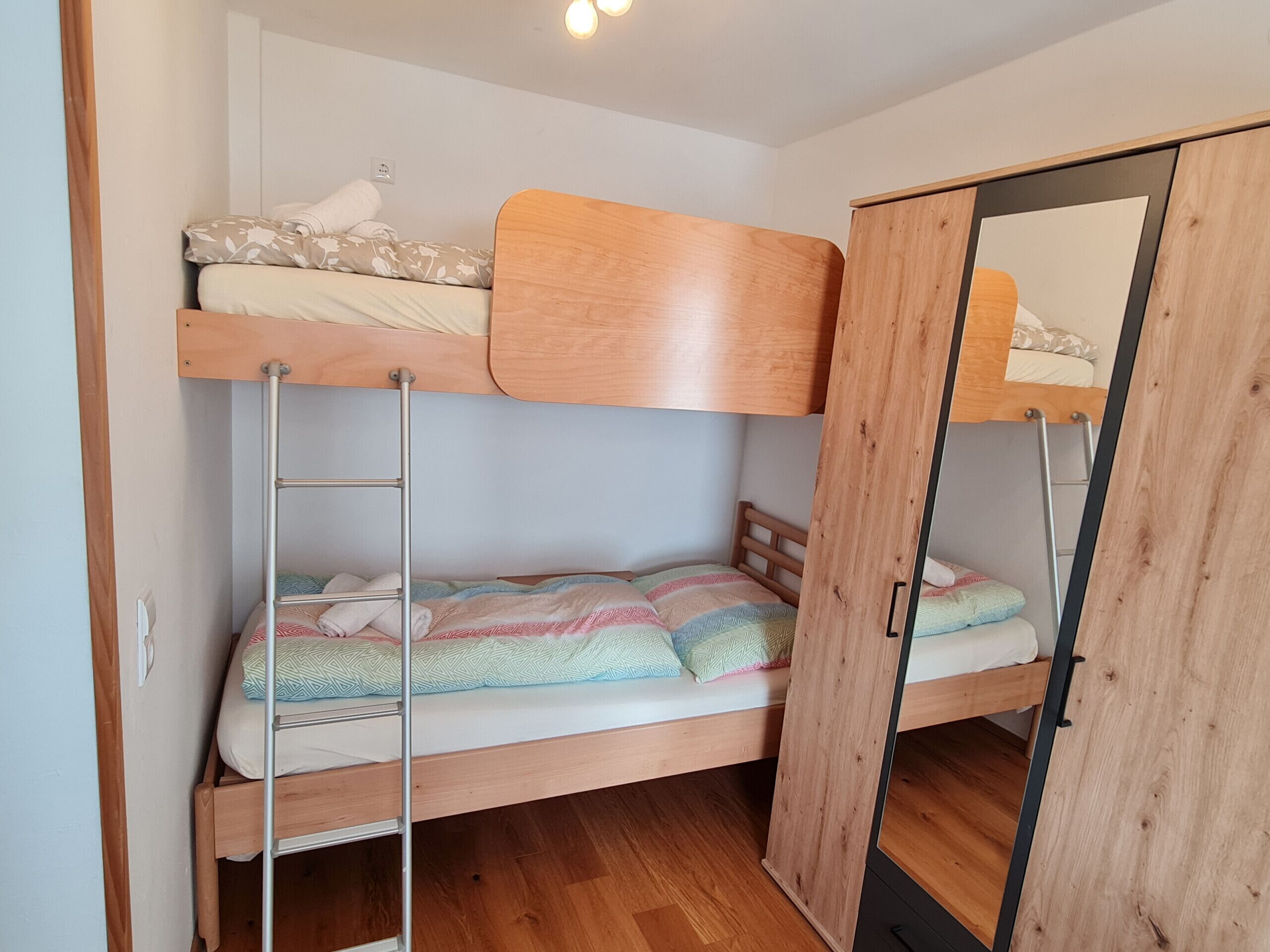 Une chambre avec un lit superposé, une échelle en bois, une armoire et un miroir.